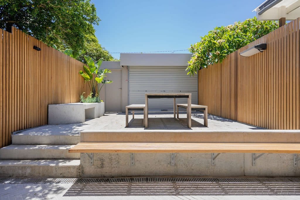 Courtyard looking towards the rear garage, with concrete steps, a timber bench and timber-batten fences