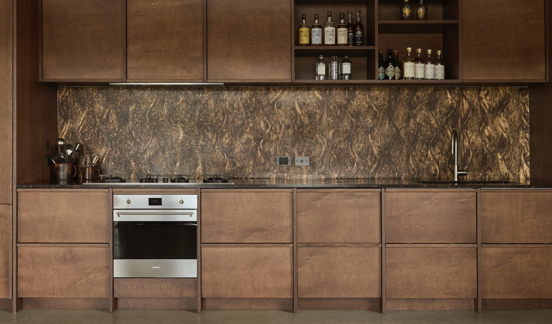 Kitchen run of dark timber cabinetry with open shelving and a textured bronze-toned splashback