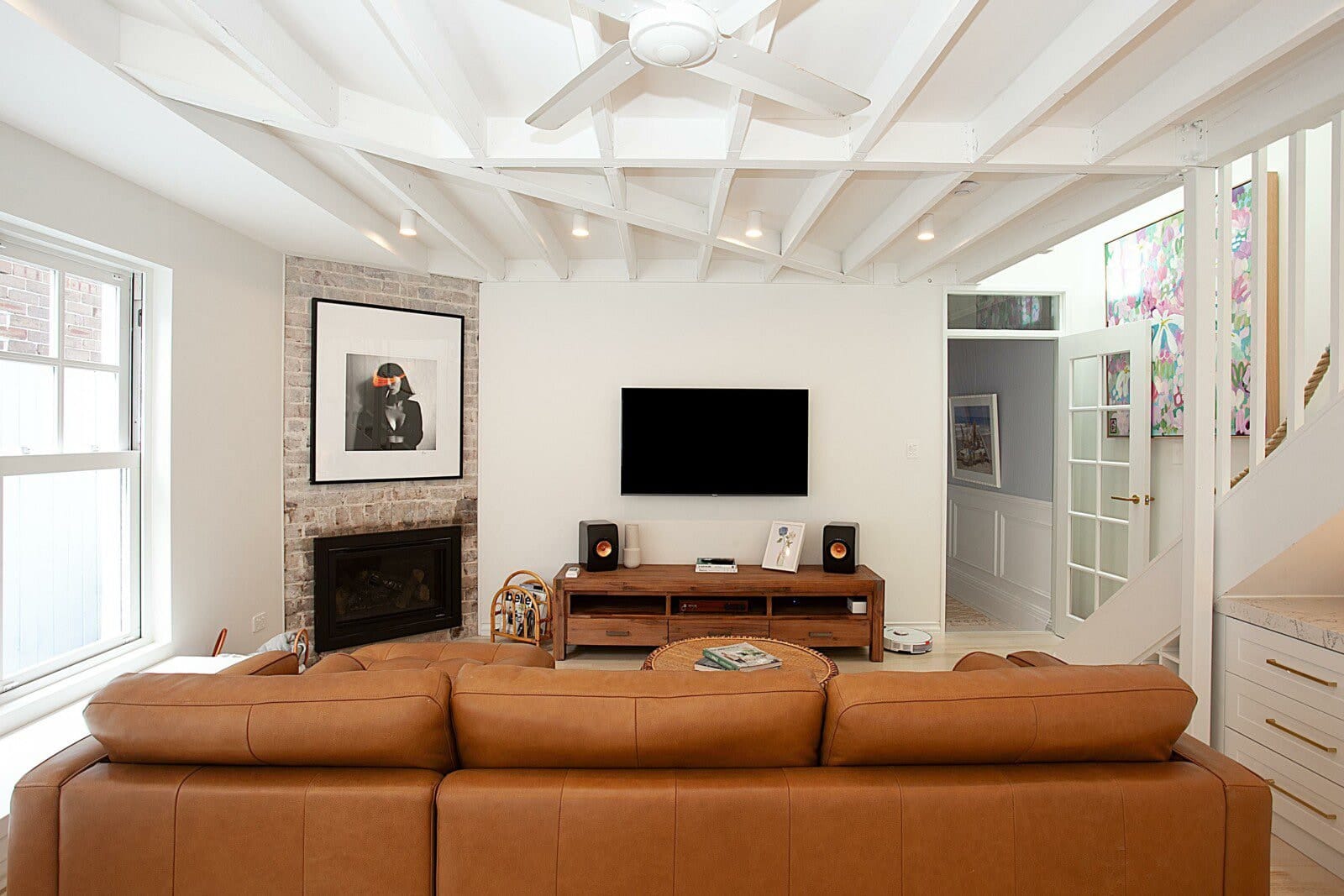 Living area with a brick fireplace surround, white ceiling joists and a tan leather sofa