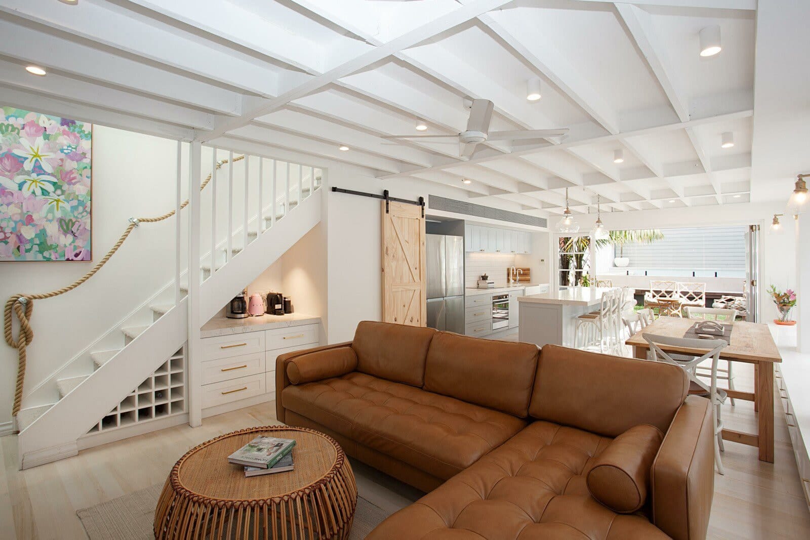 Living room with white-painted exposed ceiling joists, a tan leather sofa and an open staircase with a rope handrail