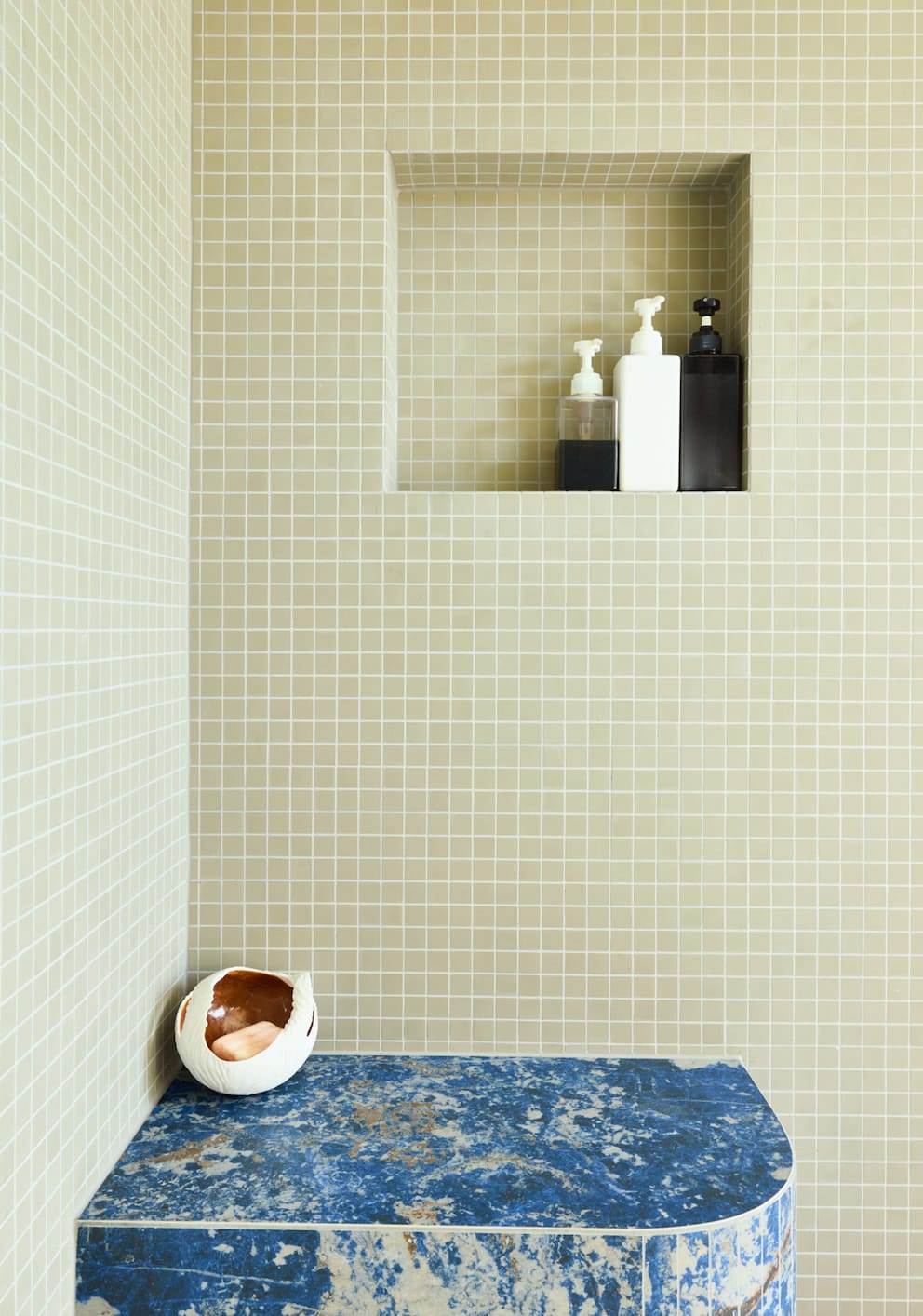Shower niche in sage mosaic tiles above a curved bench clad in blue patterned stone
